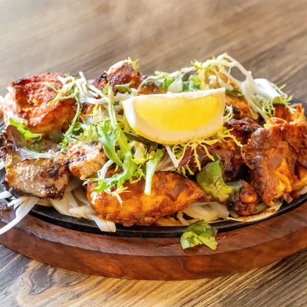 Sizzling chicken tikka, garnished with fresh lettuce and a lemon wedge, on a wooden board.