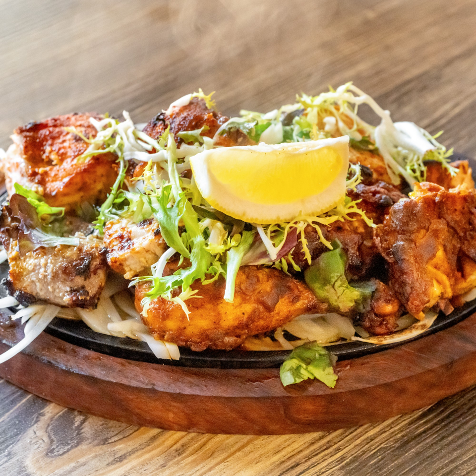 Sizzling chicken tikka, garnished with fresh lettuce and a lemon wedge, on a wooden board.