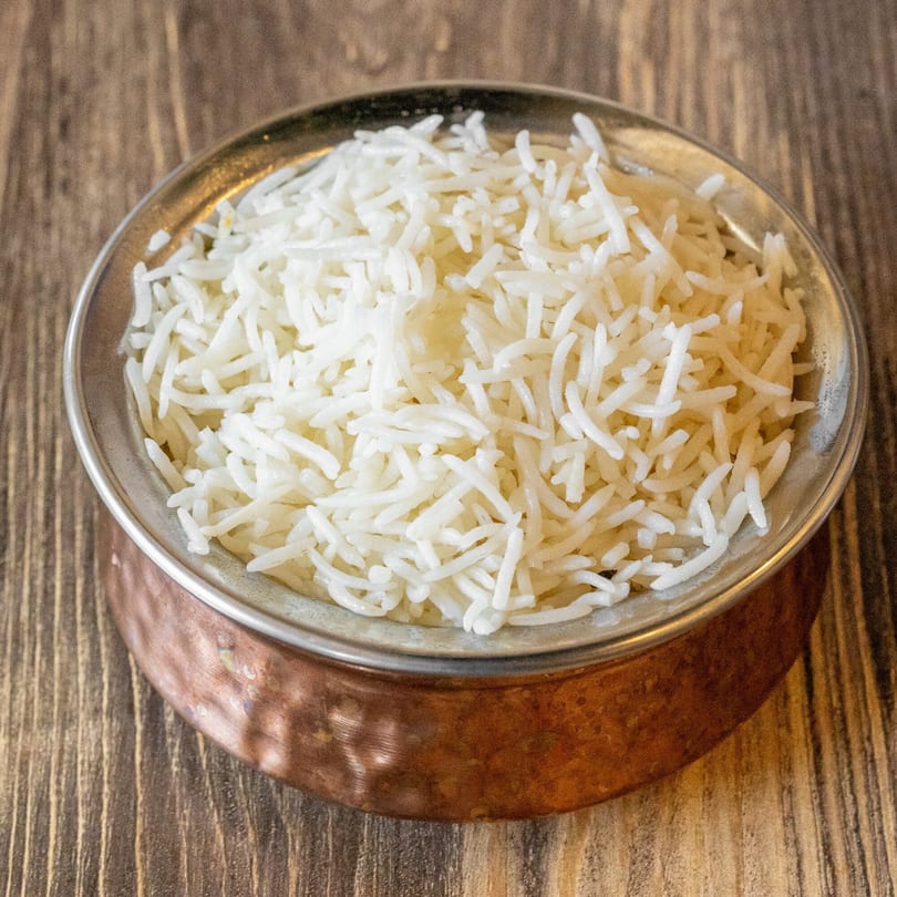 Fluffy white basmati rice served in a rustic copper bowl on a wooden table.